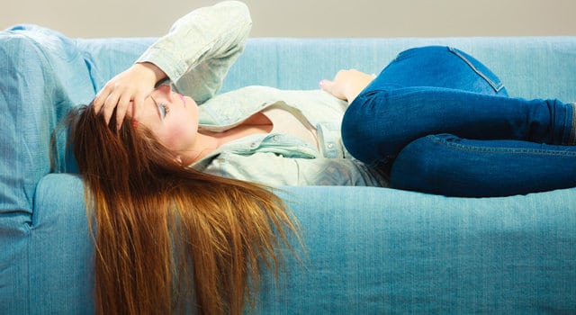 sick young woman laying on a couch 